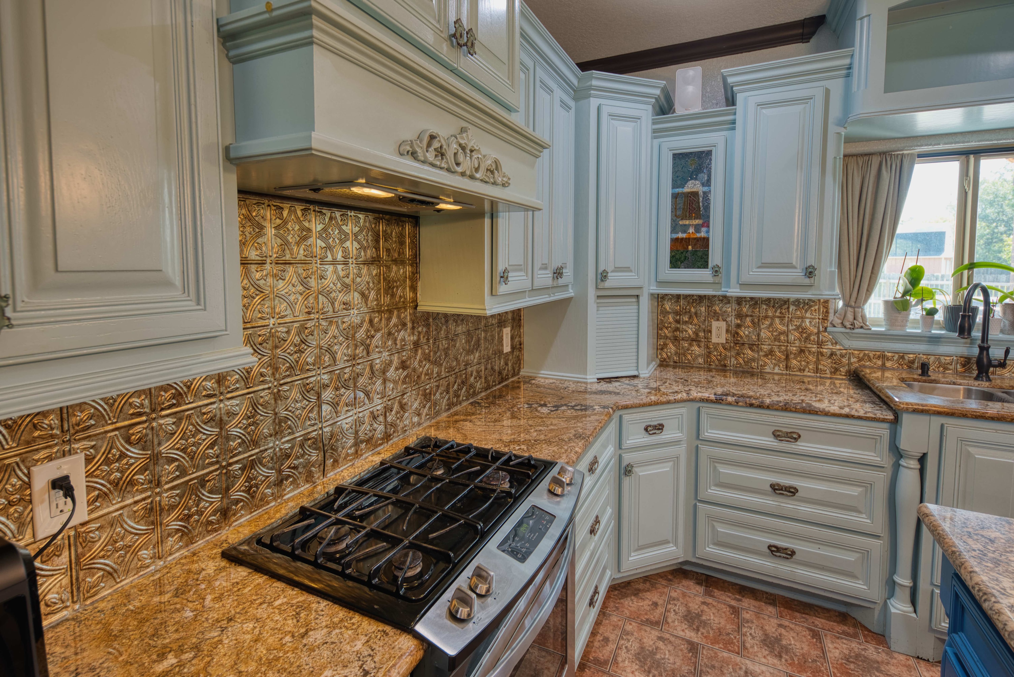 Luxury kitchen with blue cabinetry and ornate gold backsplash